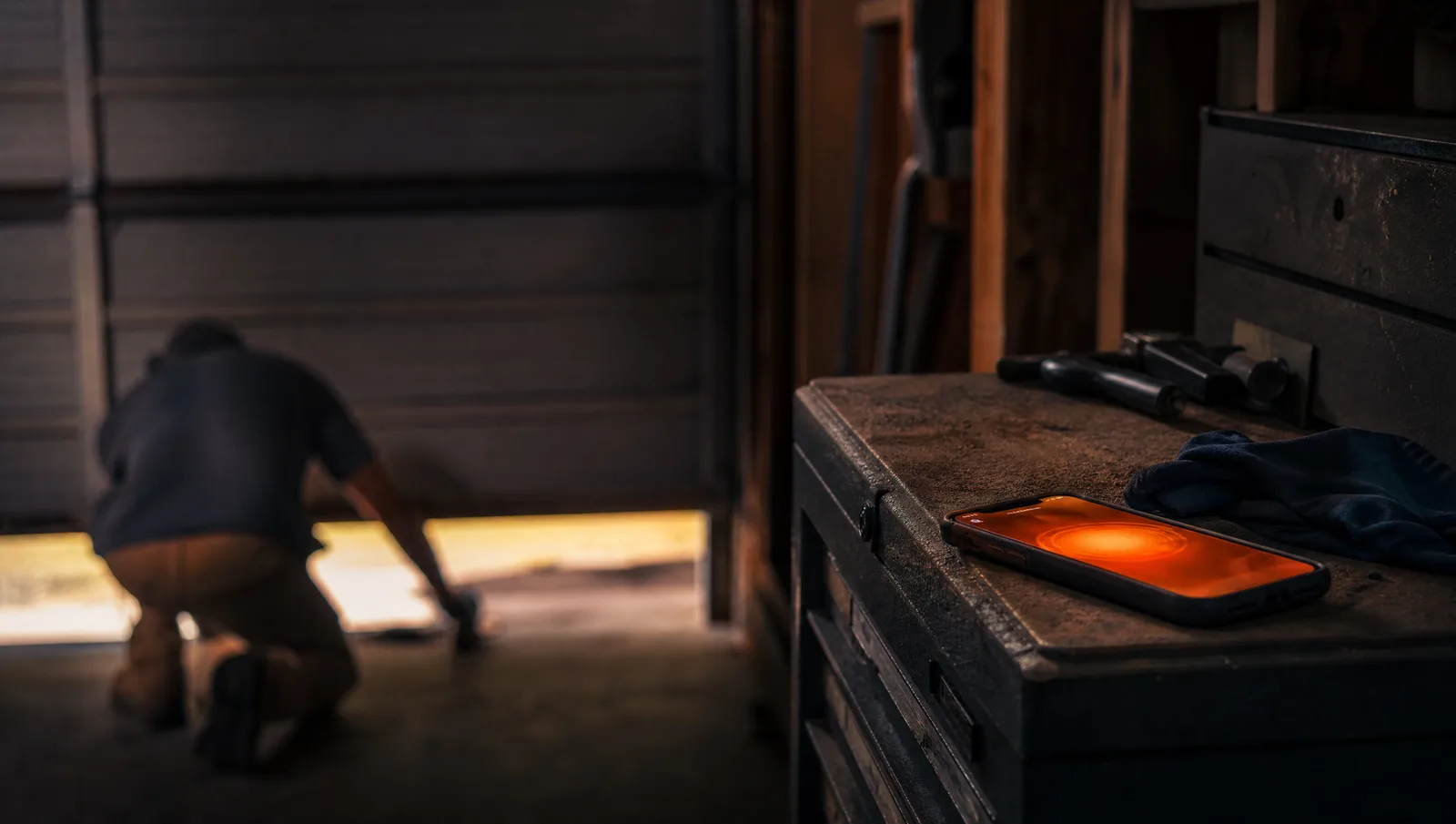 Tradesperson working on a garage door at dusk with a phone glowing on a workbench
